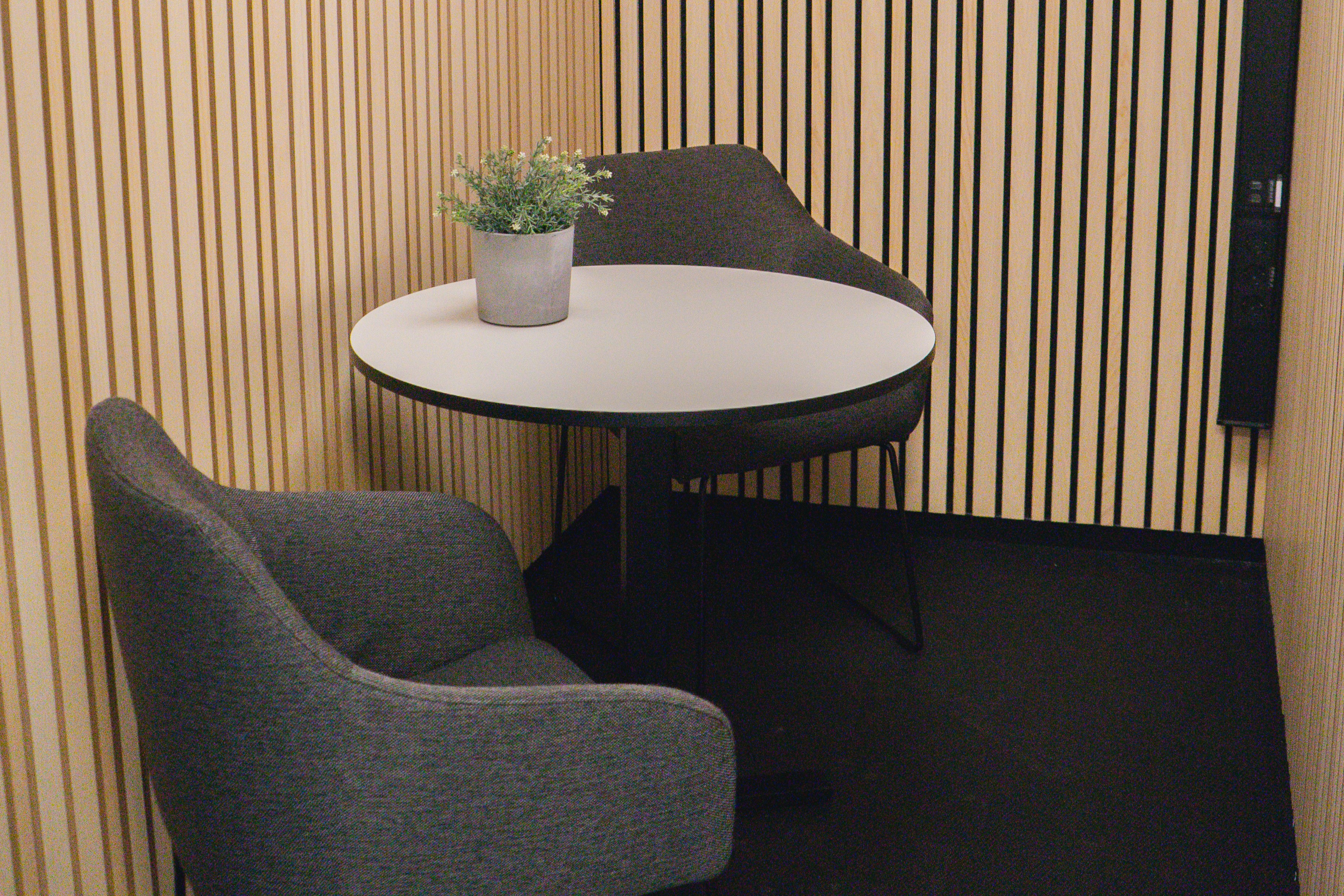 Mötesrum med två fåtöljer och ett bord, med akustikpanel på väggarna.